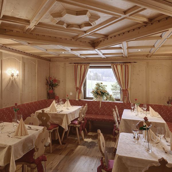 Traditional Alpine dining room with ornate wooden coffered ceiling, red patterned upholstered benches, white tablecloths, and mountain views through window