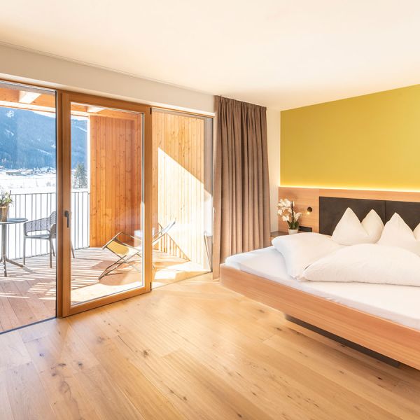 Contemporary hotel room with yellow accent wall, wooden flooring, balcony with mountain views, and modern furnishings