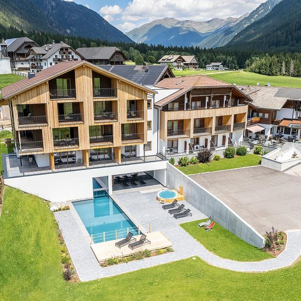 Aerial view of Alpine hotel resort with outdoor pool, surrounding green meadows, and mountain valley landscape in summer