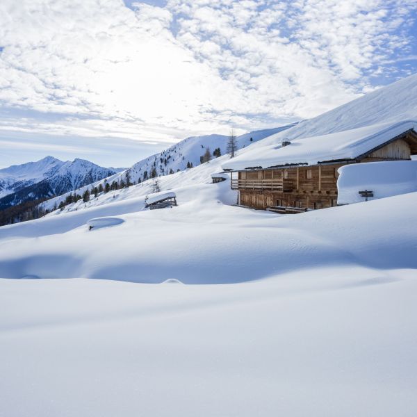 Traditional wooden Alpine chalet in deep winter snow with mountain slopes and clear blue sky