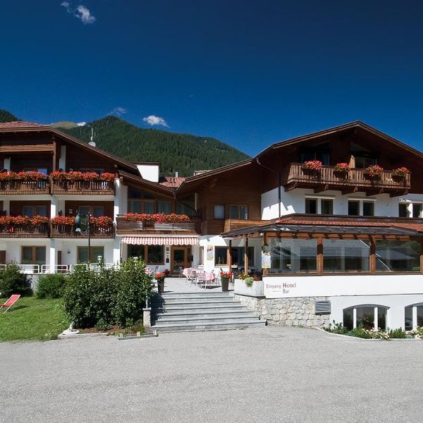 Traditional Alpine hotel with flower-decorated balconies, outdoor terrace, and green mountain meadows in summer
