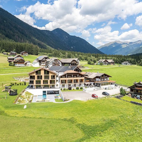 Aerial panoramic view of Alpine hotel complex nestled in green valley with surrounding mountains and traditional village