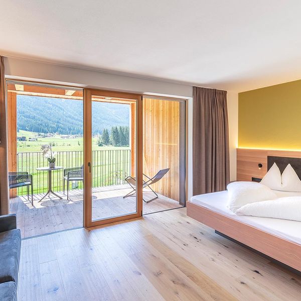 Bright modern hotel room with large balcony doors, mountain panorama, and warm wooden flooring
