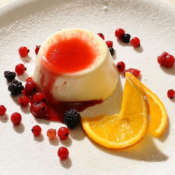 Elegant panna cotta dessert with berry coulis, fresh berries, orange slices, and powdered sugar on white plate