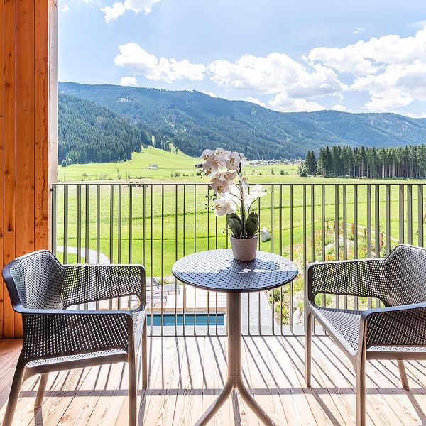 Private wooden balcony with bistro table, wicker chairs, and panoramic mountain valley views framed by rustic wood panels