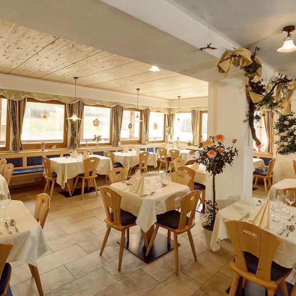 Traditional Alpine restaurant dining room with wooden ceiling, white tablecloths, rustic wooden chairs, and decorated column