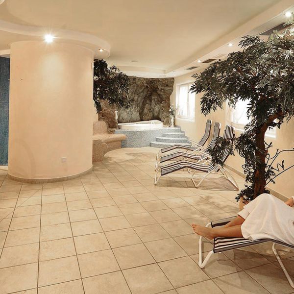 Spa relaxation lounge with striped deck chairs, decorative trees, natural stone grotto features, and tiled flooring