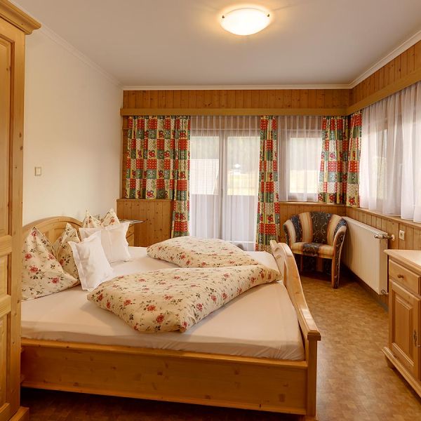 Traditional Alpine hotel room with pine wood paneling, furniture, floral patterned bedding, and colorful curtains