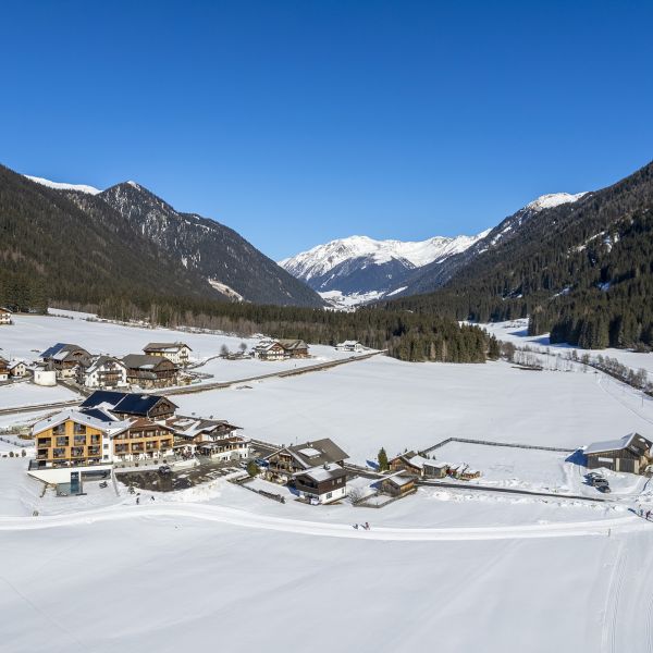 Aerial winter panorama of Alpine village hotels and chalets in snow-covered valley with mountain backdrop under clear blue sky