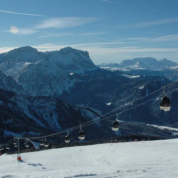Cable car gondolas ascending over groomed ski slopes with panoramic view of snow-covered Dolomite mountain ranges