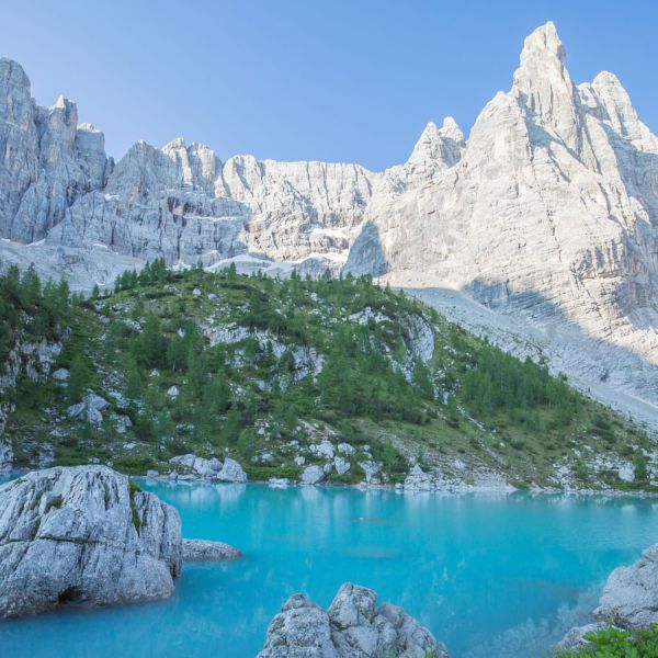 Stunning turquoise Lago di Sorapis alpine lake with dramatic white Dolomite rock formations, pine forests, and rocky shoreline