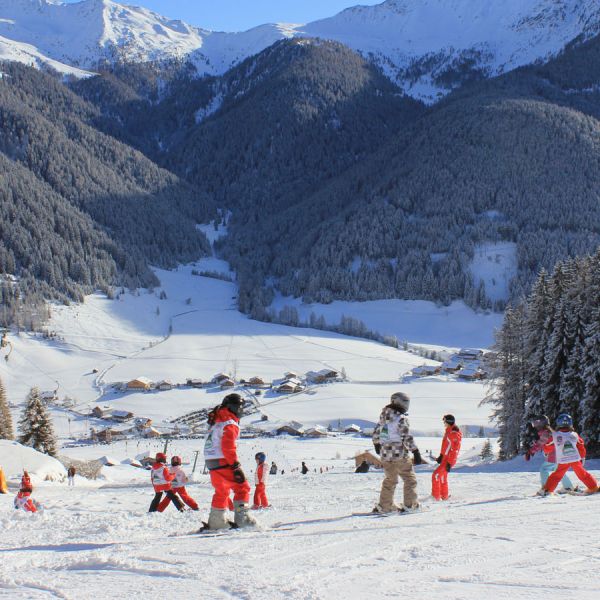 Ski school instructors in orange uniforms teaching children on sunny mountain slope overlooking valley village below