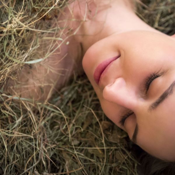 Woman lying peacefully on hay during natural wellness spa treatment with eyes closed in rustic Alpine setting