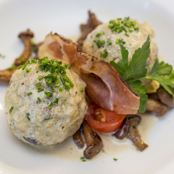 Traditional bread dumplings (Knödel) garnished with fresh chives, bacon, and sautéed mushrooms on white plate