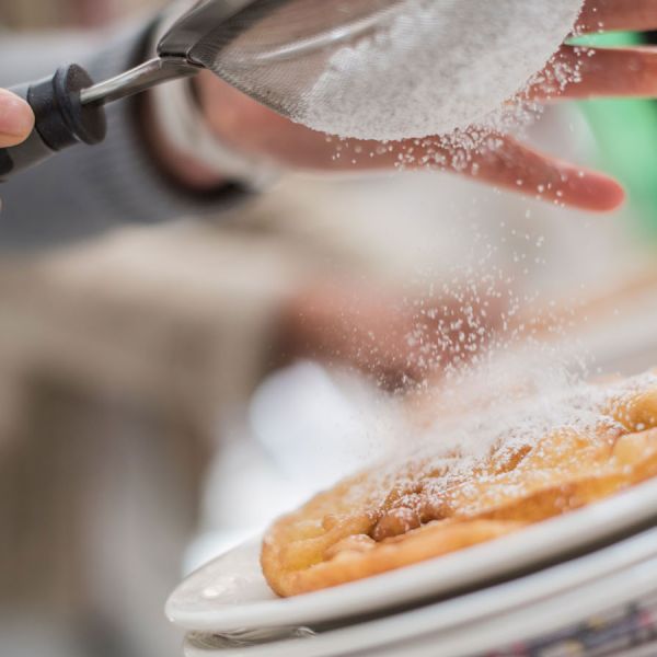 Chef's hands sprinkling powdered sugar through sieve onto fresh apple strudel pastry on white plate