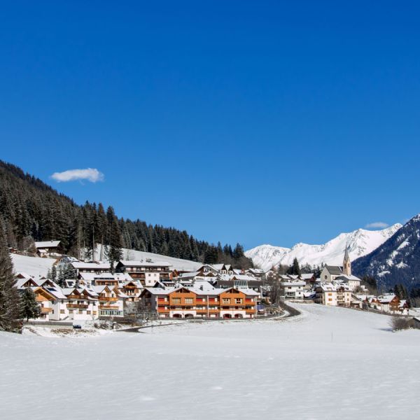 inter panorama of snow-covered Alpine village with traditional wooden chalets and dramatic snow-capped mountain peaks under clear blue sky