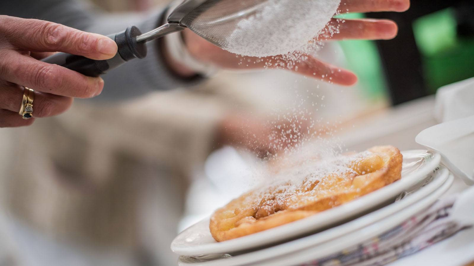 ein Mitarbeiter der Küche des Hotels Tyrol in Gsies streut Staubzucker über einen traditionellen Südtiroler Apfelstrudel