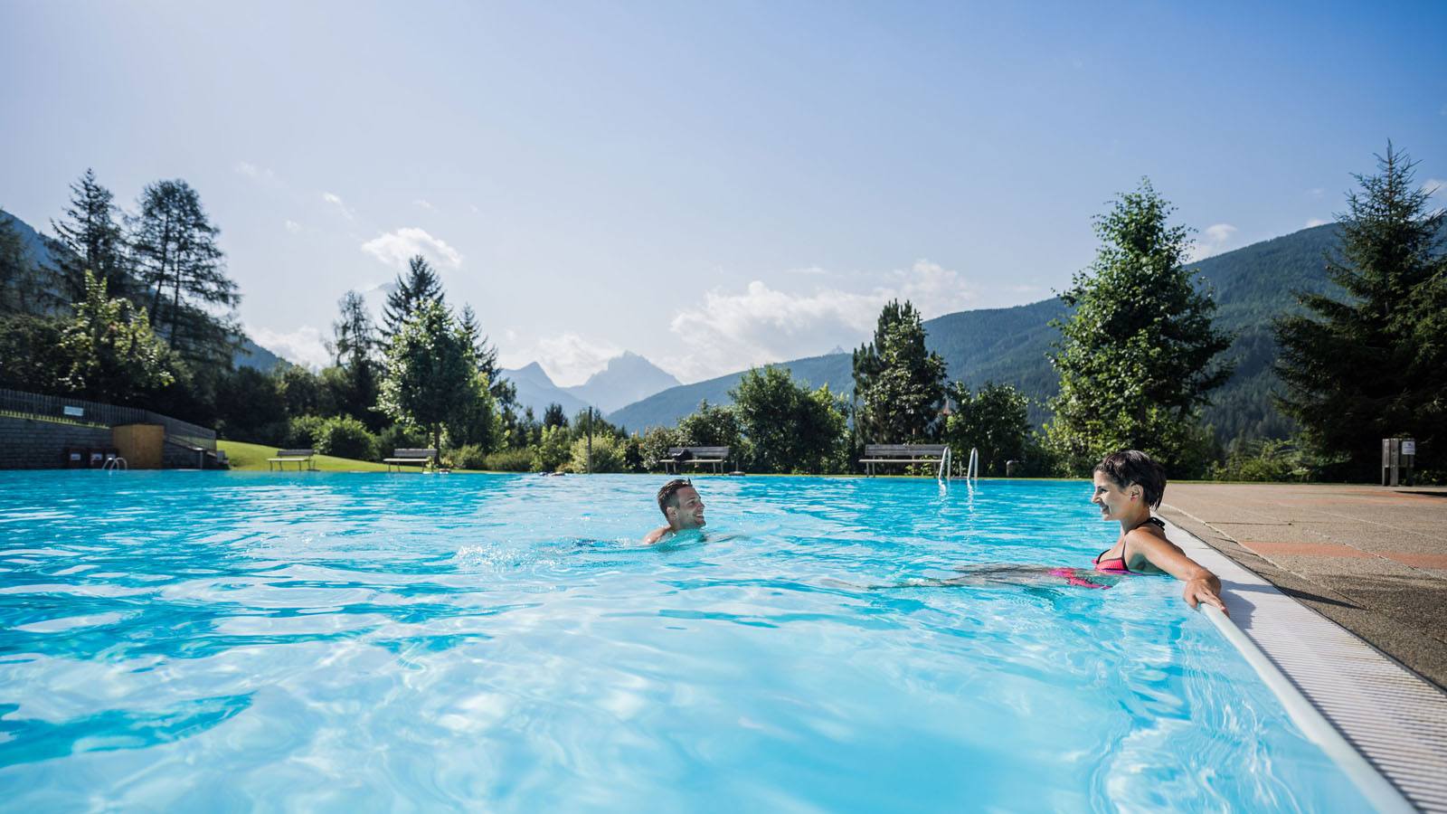 a couple enjoys the summer in the outdoor pool of the Hotel Tyrol in Casies
